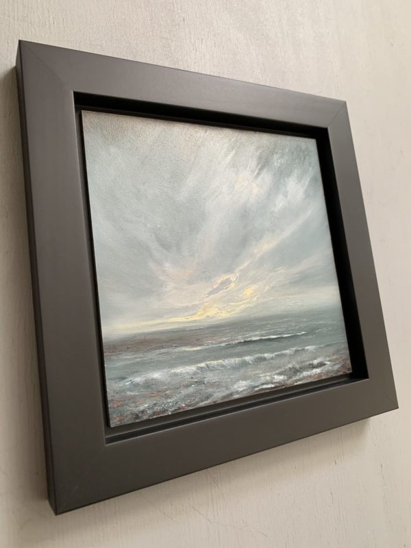 Original seascape oil painting by Tisha Mark, "The Watching" 6"x6" oil on gessobord (2024). Light emerges in a stormy sky over a stormy sea. Shown here in a black float frame at an angle from left.