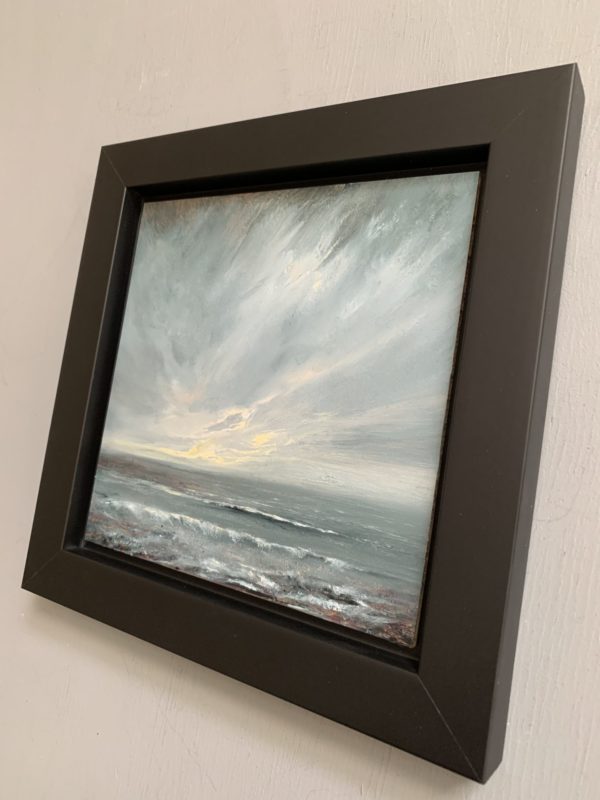 Original seascape oil painting by Tisha Mark, "The Watching" 6"x6" oil on gessobord (2024). Light emerges in a stormy sky over a stormy sea. Shown here in a black float frame at an angle from right.