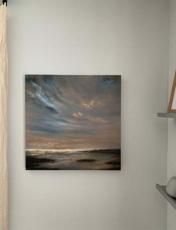 Original seascape oil painting by Tisha Mark, "Sunset on Opening Day" 20"x20" oil on linen (2024), shown here in situ. A seascape painting with dramatic blue clouds in orange-toned sunset skies over a rocky seashore. Flecks of orange light appear in the sky, and colors from the sky are reflecting in water below.