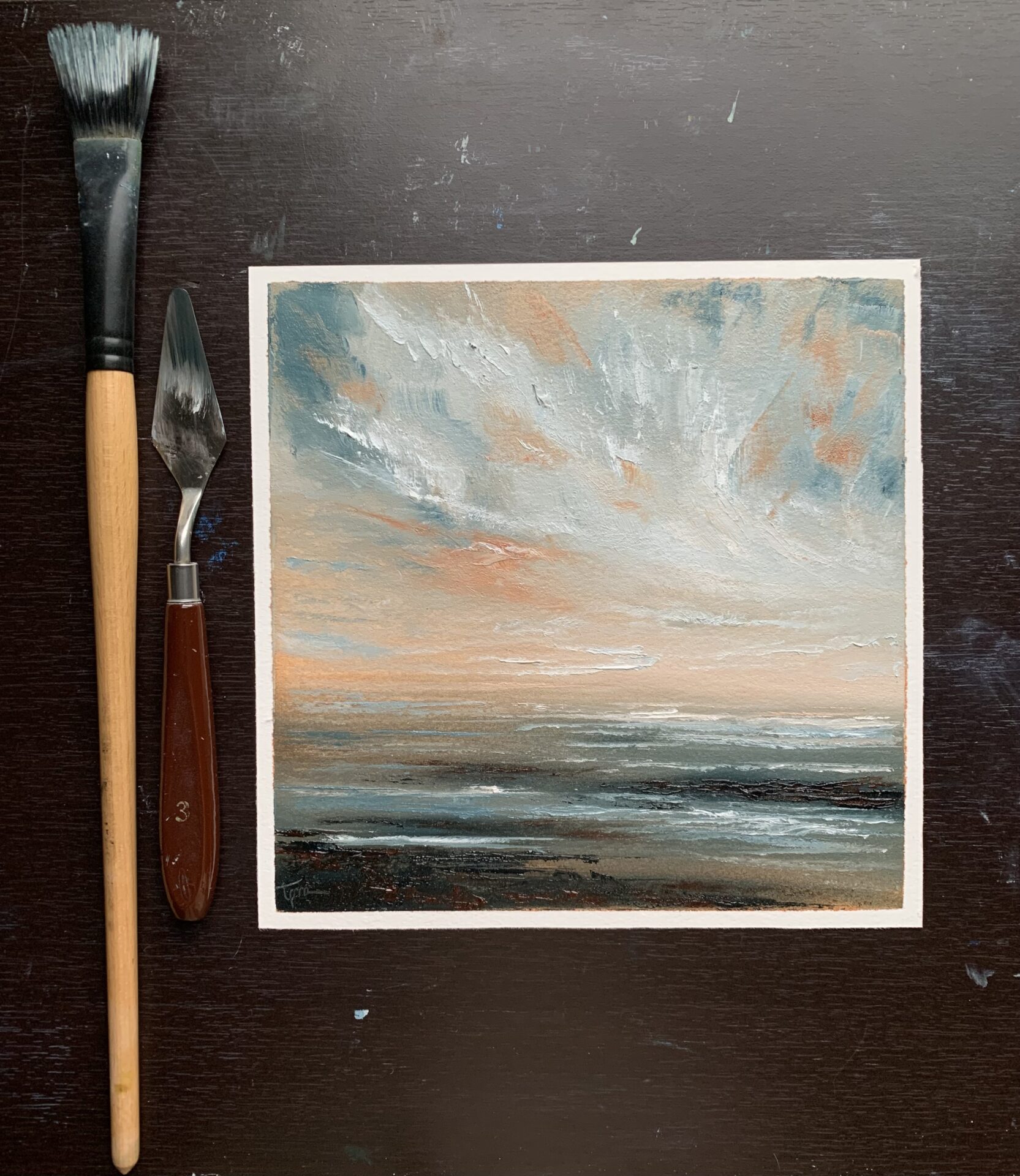 Original seascape oil painting by Tisha Mark, "Storm Light" 8"x8" oil on Arches oil paper (2024), shown here with a paintbrush and palette knife for scale.